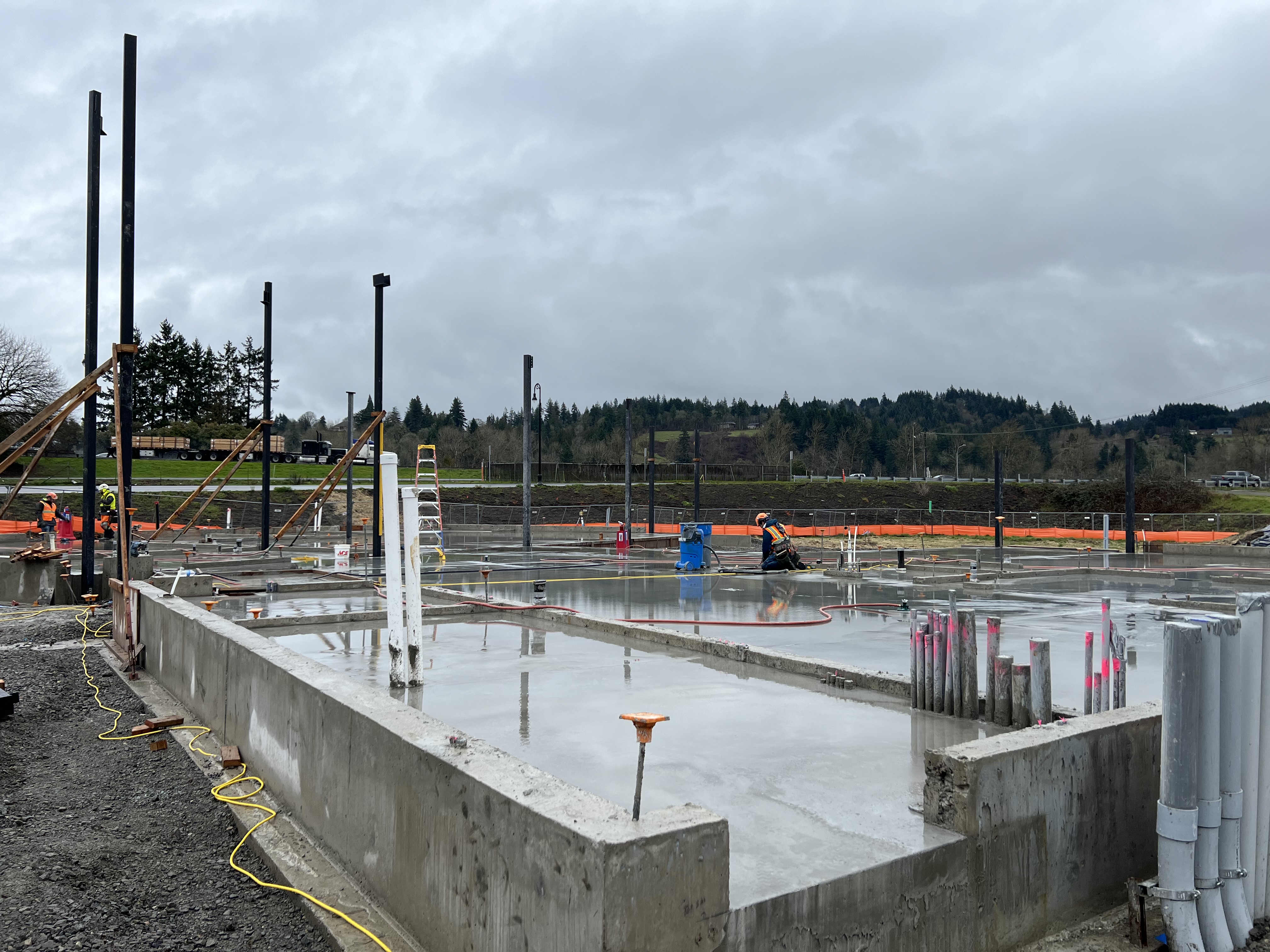 Picture of the freshly poured concrete floor of the future Woodland Community Library, slicked with rain, on a wet day