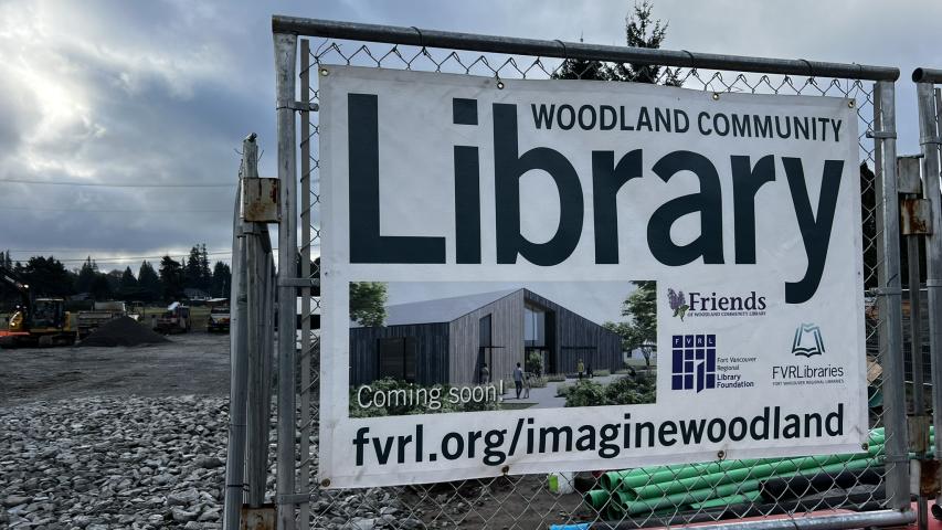 Sign posted to a chain link fence. The sign reads: "Woodland Community Library—coming soon!" 