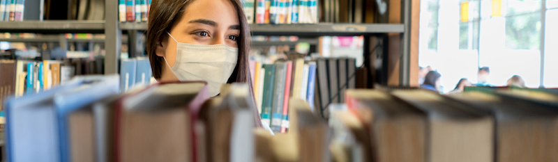 Woman wearing a mask browsing shelves in library