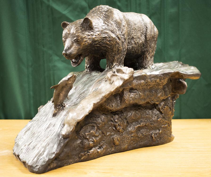 Almost - Jim Riedl A bronze sculpture of a bear trying to catch a fish leaping from a rushing river.