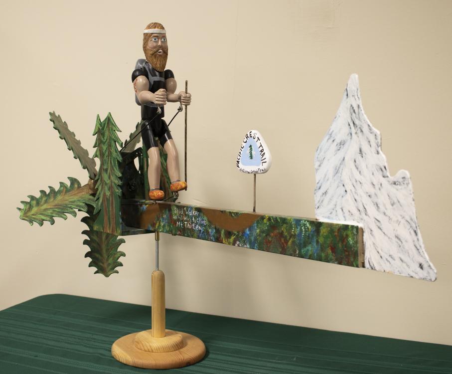 coletodd_studwalkeronhiswaytoclimbmtthielson-cw.jpg Whirligig depicting a muscular man preparing to climb a mountain.