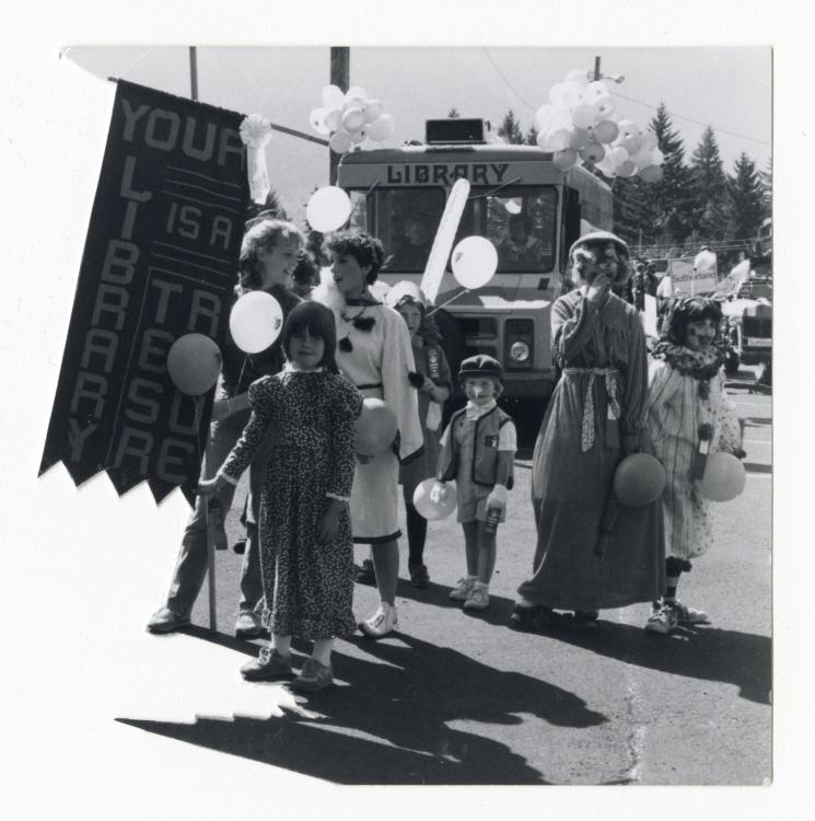 Black-and-white photo of a parade featuring a Stevenson Community Library bookmobile from the 1970s