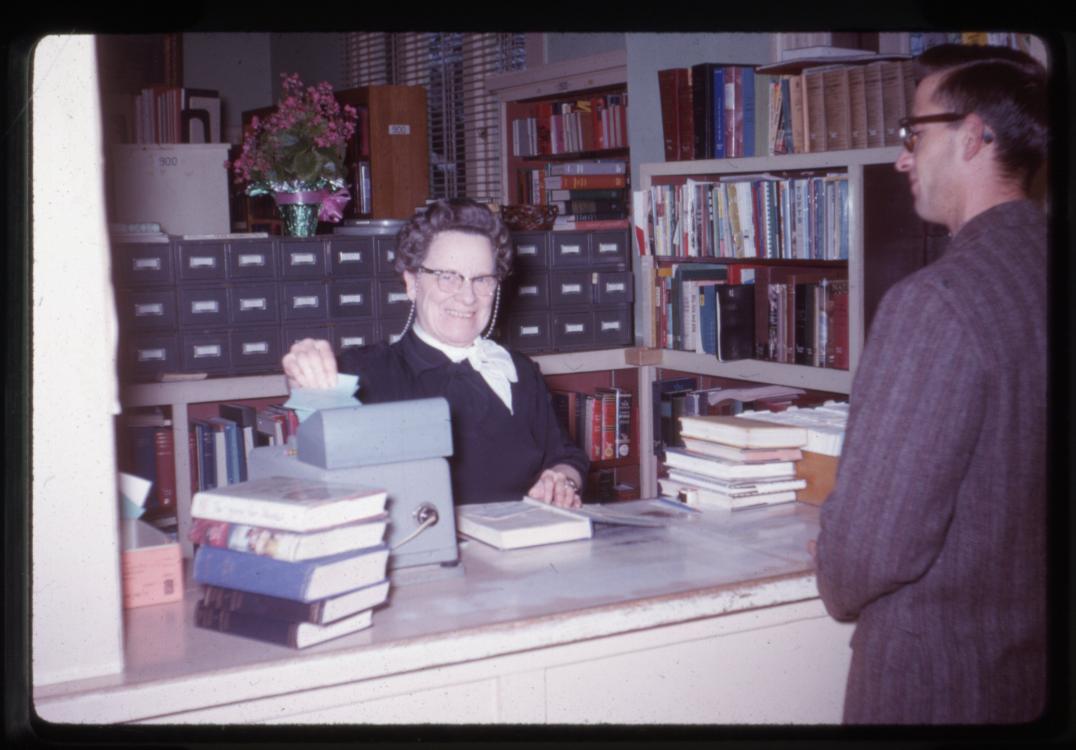 Picture of a library worker checking out materials to a patron, circa the early 1960s